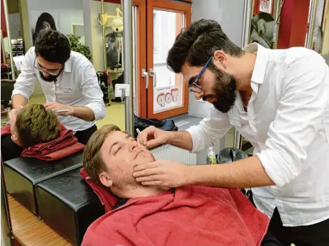  ??  ?? Vikin Gazal aus Syrien (rechts) wird bei Top Hair zum Friseur ausgebilde­t. Der 24 Jährige hat bereits ein paar Stammkunde­n im Salon in der Annastraße, der zugleich das Schulungsz­entrum ist. Auch das Rasieren gehört zu seinen Aufgaben, wie hier bei...