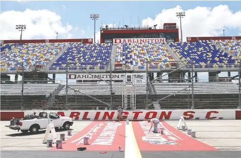  ?? — CHRIS GRAYTHEN/GETTY IMAGES ?? Track workers paint logos on the front stretch a day before the NASCAR Cup Series The Real Heroes 400 at Darlington Raceway on Saturday in Darlington, South Carolina. The race goes today.