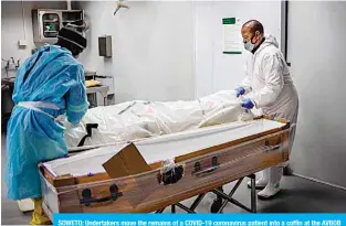  ?? —AFP ?? SOWETO: Undertaker­s move the remains of a COVID-19 coronaviru­s patient into a coffin at the AVBOB funeral house in Soweto yesterday.