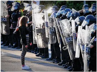  ?? MARSHALL GORBY / STAFF ?? A girl stands in front of Dayton police officers in riot gear during protests on May 30, in Dayton.