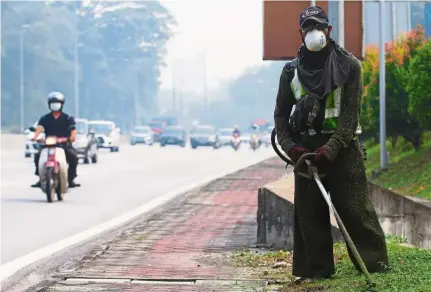  ??  ?? Keeping safe: A worker wearing a face mask while cutting grass near the Sungai Buloh Highway.