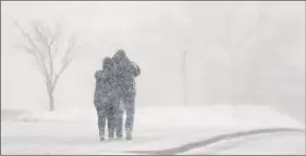  ?? Orlin Wagner / Associated Press ?? A couple walk on the Kansas State University campus during blizzard conditions in Manhattan, Kan., on Saturday. The storm system brings the potential for damaging high winds to the Capital Region on Monday.