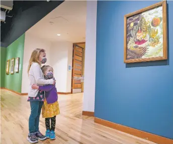  ?? PHOTOS BY GABRIELA CAMPOS/THE NEW MEXICAN ?? ABOVE: Sisters Silvie and Macie Miller of Rio Rancho look at Frida Kahlo’s painting The Love Embrace of the
Universe, the Earth (Mexico), Myself, Diego, and Señor Xolotl at the Albuquerqu­e Museum.
BELOW RIGHT: Maureen Ryan, store manager, adjusts aprons featuring Frida Kahlo in the museum’s store. BOTTOM: Lea Smith of Fort Worth, Texas, sports a Frida Kahlo mask while visiting the museum.