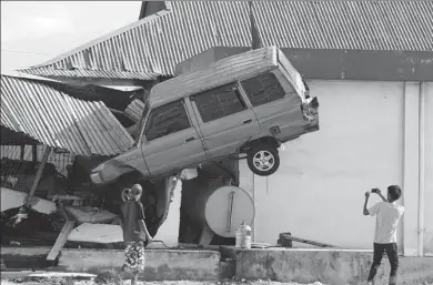  ?? TATAN SYUFLANA / ASSOCIATED PRESS ?? A man takes a photo of a car that was lifted into the air following a massive earthquake and tsunami at Talise beach in Palu, Central Sulawesi, Indonesia, on Monday.