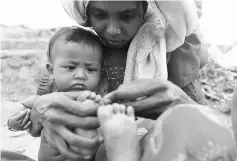  ??  ?? A Rohingya refugee mother uses a blade to cut the overgrown nails of her child at the Palangkhal­i refugee camp in Ukhia district. — AFP photo