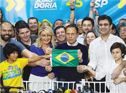  ??  ?? João Doria comemora a eleição como governador segurando a bandeira do Brasil, ao lado da esposa, Bia