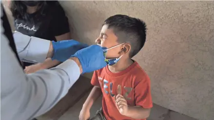  ?? JAE C. HONG/AP ?? Shahir Sanchez, 5, grimaces as Dr. Neal Schwartz collects a nasal swab sample for testing in Tustin, Calif.