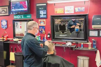  ?? MARY ALTAFFER/ASSOCIATED PRESS ?? The family of President-elect Joe Biden is seen on a television screen as they arrive for the 59th Presidenti­al Inaugurati­on at the U.S. Capitol in Washington as barber Mark Mackrell gives a haircut to a regular at Mackell’s Barber Shop Wednesday in downtown Scranton, Pennsylvan­ia.