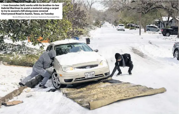  ?? Bronte Wittpenn/Austin American-Statesman/Associated Press ?? > Ivan Gonzales (left) works with his brother-in-law Gabriel Martinez to assist a motorist using a carpet to try to ascend a hill along snow-covered Cherrywood Road in Austin, Texas, on Tuesday