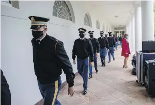  ??  ?? U.S. Army Honor Guard soldiers wearing masks walk along the colonnade to help remove the flags after U.S. President Donald Trump spoke at a press briefing at the White House.