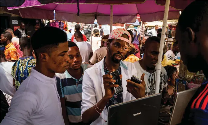  ??  ?? Ola Mide (middle), a vendor in the Computer Village market in Lagos, Nigeria. He sells music that he downloads from the internet