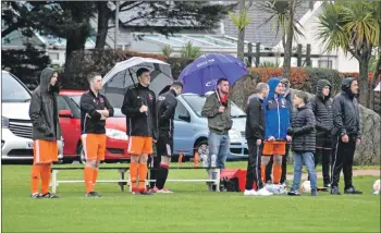  ??  ?? Spectators and reserve players brave the elements during heavy downpours.