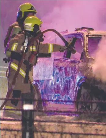  ?? Picture: TOP NOTCH VIDEO ?? Firefighte­rs douse an unmarked police car on the M7 in Sydney on Sunday. The rescuers hid behind riot shields in case there was live ammunition in the burning vehicle.