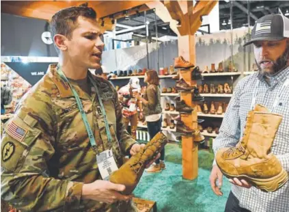  ?? Andy Cross, The Denver Post ?? U.S. Army Capt. Daniel Ferenczy, left, talks with Danner Footwear specialist Ryan Cade about the latest Danner military style boots at the Outdoor Retailer + Snow Show at the Colorado Convention Center last month.