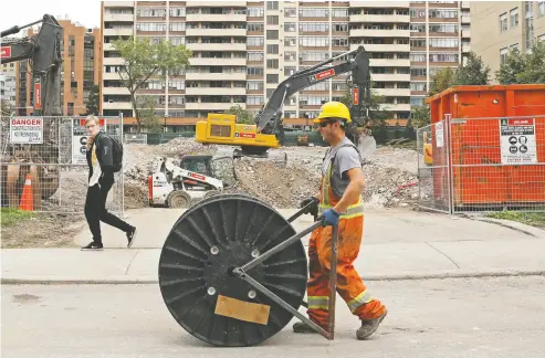  ?? CHRIS HELGREN / REUTERS ?? A worker passes a constructi­on site with a roll of cable in Toronto on Friday. While highly skilled and highly paid workers are doing better than they did before the pandemic, experts say lower-paid workers were left behind.