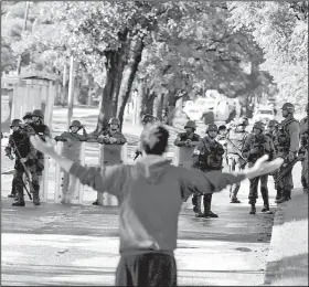  ?? AP/JUAN CARLOS HERNANDEZ ?? A man confronts a line of Venezuelan national guardsmen Sunday outside the Paramacay military base in the city of Valencia near Caracas, where armed assailants reportedly were repelled after a pre-dawn attack.