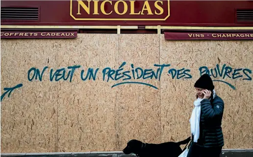  ??  ?? A woman walks by a graffiti on a wine shop reading ‘We want a president for the poor’, near the Arc de Triomphe, in Paris. A protest against rising taxes and the high cost of living turned into a riot in the French capital at the weekend, as activists caused widespread damage and tagged the Arc de Triomphe with multi-colored graffiti during clashes with police.
