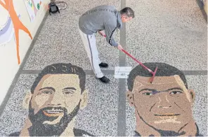  ?? AFP ?? Kosovar artist Alkent Pozhegu works on the last details of a mosaic, made with grain and seeds on the ground, depicting Argentina’s Lionel Messi, left, and France’s Kylian Mbappe.