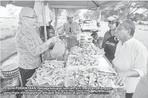  ?? — Gambar Bernama ?? PENUHI PERMINTAAN: Peniaga ketupat Jamilah (kiri) melayan pelanggan yang ingin mendapatka­n ketupat daun palas di gerainya.