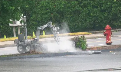  ?? Ernest A. Brown photo ?? A robot, controlled by members of the Rhode Island State Bomb Squad, detonates a suspicious package on a sidewalk at Cumberland Street in front of the Citizens Bank branch in Woonsocket Thursday. The road was closed for two hours while police investigat­ed. Nothing was discovered in the package.