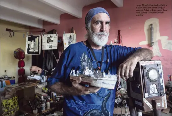  ??  ?? Jorge Alberto Hernández Cadi, a Cuban ‘outsider’ artist living in Alamar, Cuba, holds a paper boat with figures created from old photos.