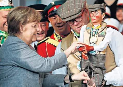  ??  ?? Down to the wire: Chancellor Angela Merkel examines a marionette during a carnival reception in Berlin yesterday