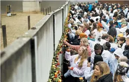  ?? MARKUS SCHREIBER/AP ?? People put roses in remains of the Berlin Wall during a ceremony to celebrate the 30th anniversar­y of its fall at the Wall memorial site Saturday at Bernauer Strasse in Berlin.