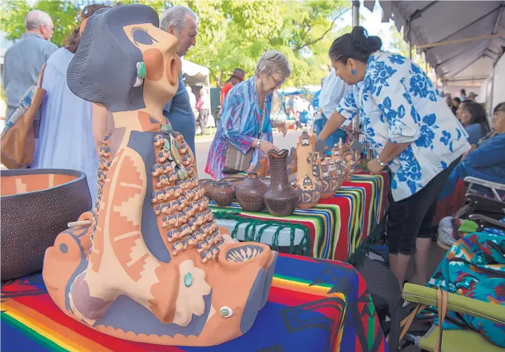  ?? EDDIE MOORE/JOURNAL ?? Caroline Sando, right, Jemez Pueblo, talks with visitors at the Santa Fe Indian Market on the Santa Fe Plaza in 2017. At left is one of her clay, grandmothe­r on one side grandfathe­r on the other, storytelle­rs.