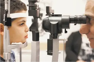  ?? Bill West / Associated Press ?? Dr. Albert Maguire checks the eyes of Misa Kaabali, 8, at the Children’s Hospital of Philadelph­ia. Misa was 4 years old when he received his gene therapy treatment.