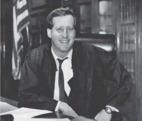  ?? BOSTON HERALD FILE ?? THROWING HIS HAT IN THE RING: Judge Mark Lawton, seen behind the bench in Juvenile Court in downtown Boston in 1991, is now running for mayor of Brockton. Below, a U.S. flag flies at half-staff outside Brockton City Hall honoring Brockton Mayor Bill Carpenter after his death at age 62 in July.