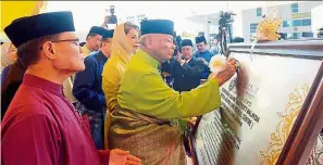  ?? — Bernama ?? It’s official: Sultan Ahmad Shah signs the plaque to commemorat­e the opening of the medical centre. looking on are Sultanah Kalsom and Adnan (left).