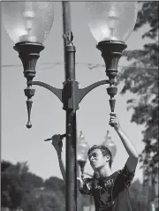  ?? AP/The Herald-Palladium/DON CAMPBELL ?? Ezra Troyer, a cross-country team member, paints a light post Friday in Watervliet, Mich., as the city held a community service day during which athletes, coaches and city workers spruced up public areas in town.