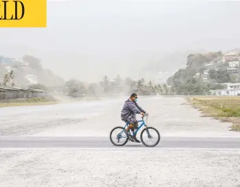  ?? LUCANUS OLLIVIERRE / AP PHOTO ?? A cyclist rides past fields covered with ash on Sunday, a day after the La Soufriere volcano erupted in Kingstown, on the eastern Caribbean island of St. Vincent. Some houses on the island have collapsed due to the weight of the ash.