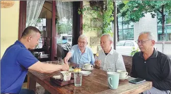  ?? CHEN ZIWEI / XINHUA ?? Li Shihong (left) chats with relatives and friends at his cafe in Xinglong, Wanning, Hainan province, last month.