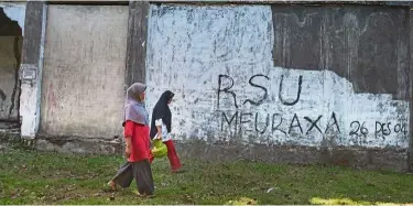  ??  ?? Timely reminder:
Women walking by a derelict building with grafiti dedicated to the 2004 Indian Ocean earthquake and tsunami in banda aceh. —aFP