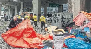  ?? CHRIS YOUNG THE CANADIAN PRESS FILE PHOTO ?? City workers move to clear a homeless encampment on Bay Street in May, as part of Toronto’s COVID-19 strategy. It appears to have worked, with just a handful of deaths among the homeless.