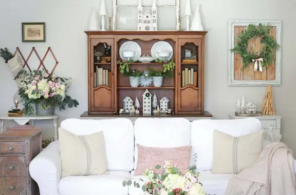  ??  ?? |TOP| BLUSH AND BEAUTIFUL. A hutch from Facebook Marketplac­e is the focal point of this half of the living room. Blush accents such as pillows and throw blankets carry the holiday color palette to this side of the space, along with bits of greenery on the back wall.