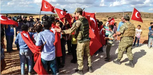  ??  ?? Children wave Turkish national flags near soldiers during a demonstrat­ion on Tuesday in support of the Turkish army’s Idlib operation near the Turkey-Syria border near Reyhanli, Hatay. (AFP)