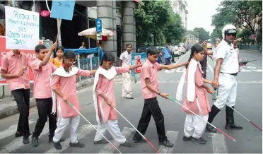  ?? — ABHIJIT MUKHERJEE ?? A policeman helps visually- challenged students cross a road on the occasion of World Sight Day in Kolkata on Thursday.