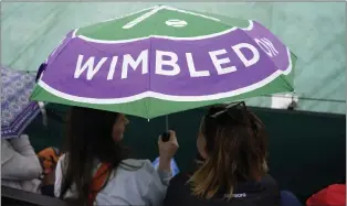  ?? KIRSTY WIGGLESWOR­TH — THE ASSOCIATED PRESS ?? Spectators sit under an umbrella on a covered court after rain delayed the start of play on Wednesday.