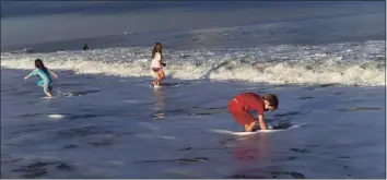  ?? Mark Makela / Getty Images ?? Rheya Long, 6, Cicely Somers, 8, and Hal Somers, 6, play with the waves on Thursday in Rehoboth Beach, Delaware. The Center for Disease Control issued a recommenda­tion urging people to stay at home and not travel for the holiday.