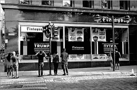  ?? MARKUS SCHREIBER/ASSOCIATED PRESS ?? A store’s poster welcoming leaders Donald Trump and Vladimir Putin draws onlookers Saturday in downtown Helsinki. The presidents are to meet Monday.