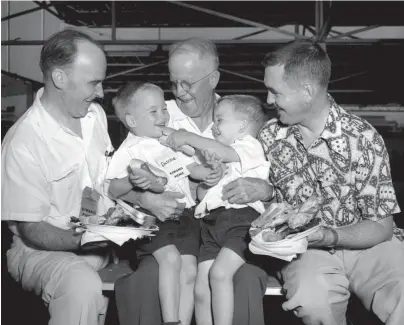  ?? THE COMMERCIAL APPEAL ?? While Kiwanians frolicked at Rainbow Lake on July 23, 1952, Edgar Butler clutched this double handful of 4-year-old grandsons, Donnie Bailey and Ronnie Bailey, sons of Mr. and Mrs. Robert S. Bailey. John Cleghorn (left), president of the Memphis Kiwanis Club, and Joe Ward neglected heaped plates to watch the dogfight (hot dogs of course), which took place at the annual Kiwanis picnic.