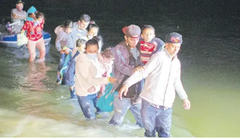  ?? AP ?? In this March 24 photo, migrant families, mostly from Central American countries, wade through shallow waters after being delivered by smugglers on small inflatable rafts on US soil in Roma, Texas.