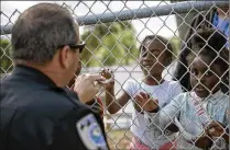  ??  ?? Capt. Mike Deighan hands police stickers to children at the YWCA Child Care Center during the march, which was attended by police, clergy, and members of the community to encourage residents to come forward with informatio­n if they witness any crimes.