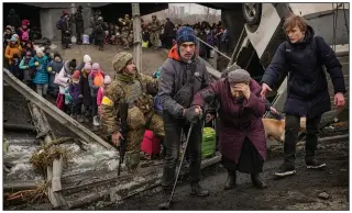  ?? (AP/Vadim Ghirda) ?? An elderly woman is assisted March 5 while crossing the Irpin River on an improvised path under a bridge that was destroyed by Ukrainian troops designed to slow any Russian military advance while fleeing the town of Irpin, Ukraine.