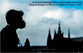  ?? (AFP) ?? A tourist wearing a face mask walks across the Charles Bridge on March 12, 2020 in Prague.