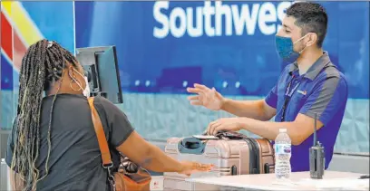  ?? The Associated Press file ?? Southwest Airlines employee Oscar Gonzalez assists a passenger at the ticket counter at Love Field in Dallas in June. The airline decided that it is not going to furlough workers in 2021 after all. A new coronaviru­s aid package includes $15 billion for airlines.