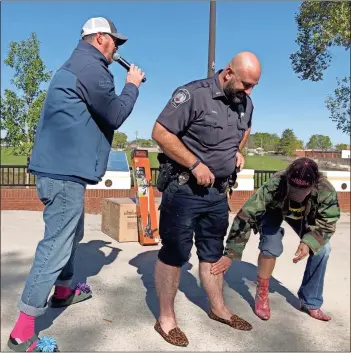  ?? K.T. Mckee ?? A representa­tive from the Hospitalit­y House checks out the winning gams of Rome officer Ryan Harris during the “hairiest legs” contest at the “Walk a Mile in Her Shoes” as Robert Smyth serves as emcee. Harris won a weed trimmer donated by Lowe’s.