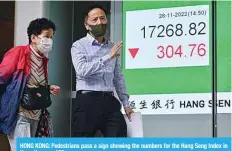  ?? ?? HONG KONG: Pedestrian­s pass a sign showing the numbers for the Hang Seng Index in Hong Kong. —AFP